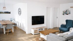 Ett modernt vardagsrum med en platt-TV, ett soffbord i trä, en grå soffa och en blå fåtölj.