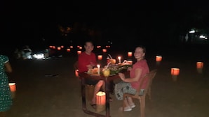 A dining table set outdoors with candles, surrounded by people. - Nilaveli Beach Rooms (Nilaveli)