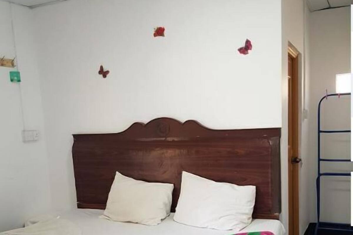 A neatly made bed with white linens and a colorful blanket, a wooden headboard, and a small butterfly decoration on the wall.