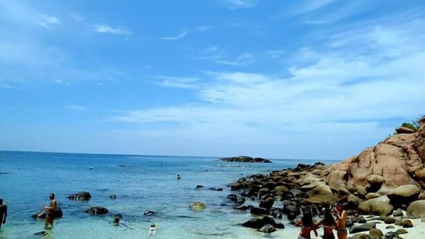 A beach with clear water, rocks, and people swimming. - Nilaveli Beach Rooms (Nilaveli)