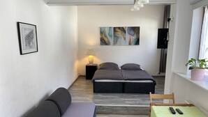 A compact hotel room with a bed, a sofa, a small table, and a potted plant.