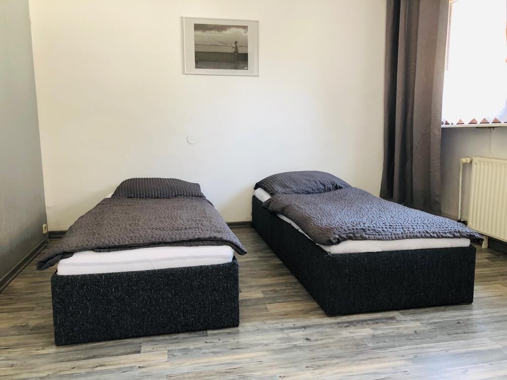 Two single beds with dark headboards and footboards in a room with a wooden floor and a framed picture on the wall.