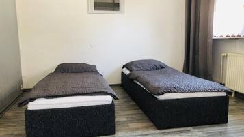 Two single beds with dark headboards and footboards in a room with a wooden floor and a framed picture on the wall.
