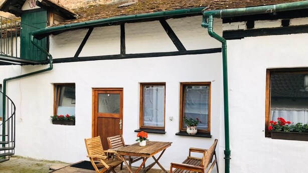 A white building with a wooden deck, a table with chairs, and flower boxes on the windowsills.