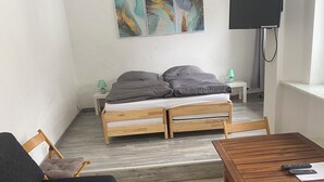 A small, cozy room with a bed, a desk, and a TV. There are two lamps on the nightstands.