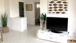 Ein modernes Wohnzimmer mit Fernseher, weißer Unterhaltungseinheit und einem Wandbild mit Fischen.