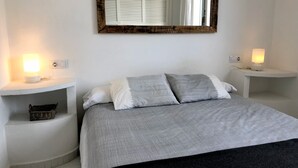 Ein Schlafzimmer mit einem Bett, zwei Nachttischen, einem Spiegel und einer Wandleuchte.