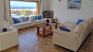 Uma sala de estar com uma janela grande, um sofá, uma mesa de centro e uma televisão.