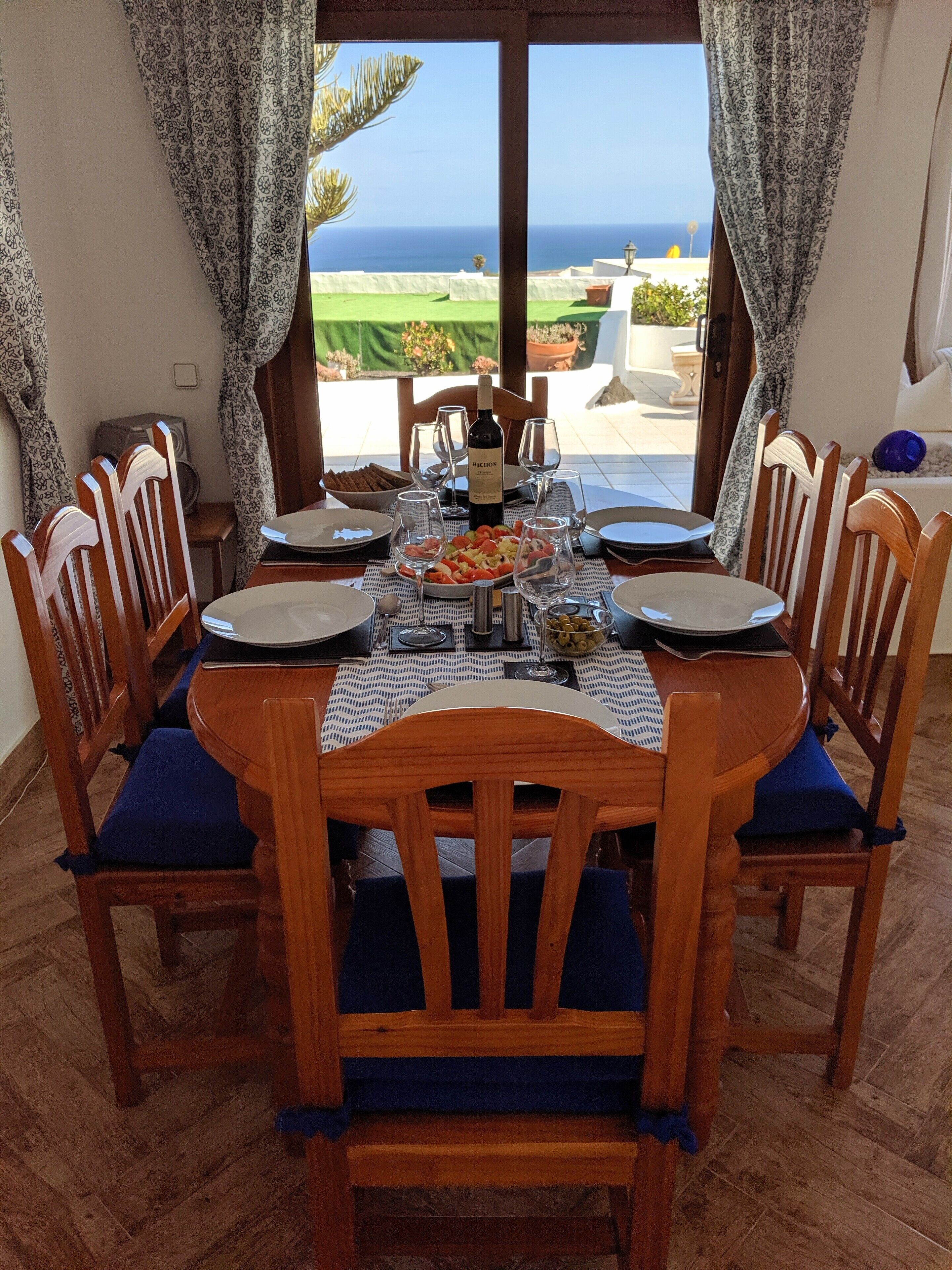 A dining table set for six with a bottle of wine, plates, and glasses.
