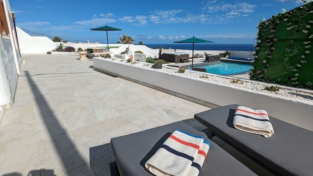 Uma área à beira da piscina com espreguiçadeiras, piscina e vista para o mar.