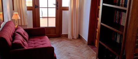 A room with a herringbone wooden floor, a red sofa, a wooden bookshelf, and a door leading outside.