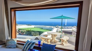 Quarto com uma grande janela com vista para a costa, incluindo um espaço de estar com almofadas e uma pequena mesa.