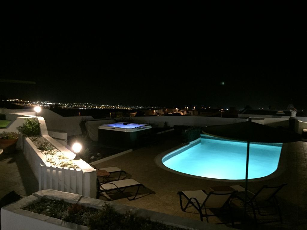 Ein Poolbereich bei Nacht mit Whirlpool, Liegestühlen und Blick auf die Stadtlichter im Hintergrund.