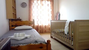 A bedroom with a wooden bed, a crib, a wardrobe, and a window with curtains. - Pelo Appartment corfu (Corfu)