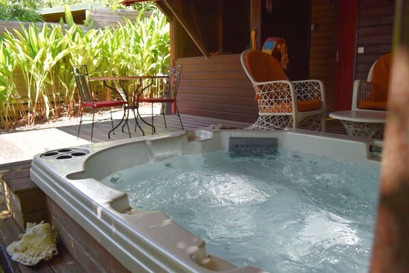 A hot tub with a wooden deck, surrounded by chairs and a table.