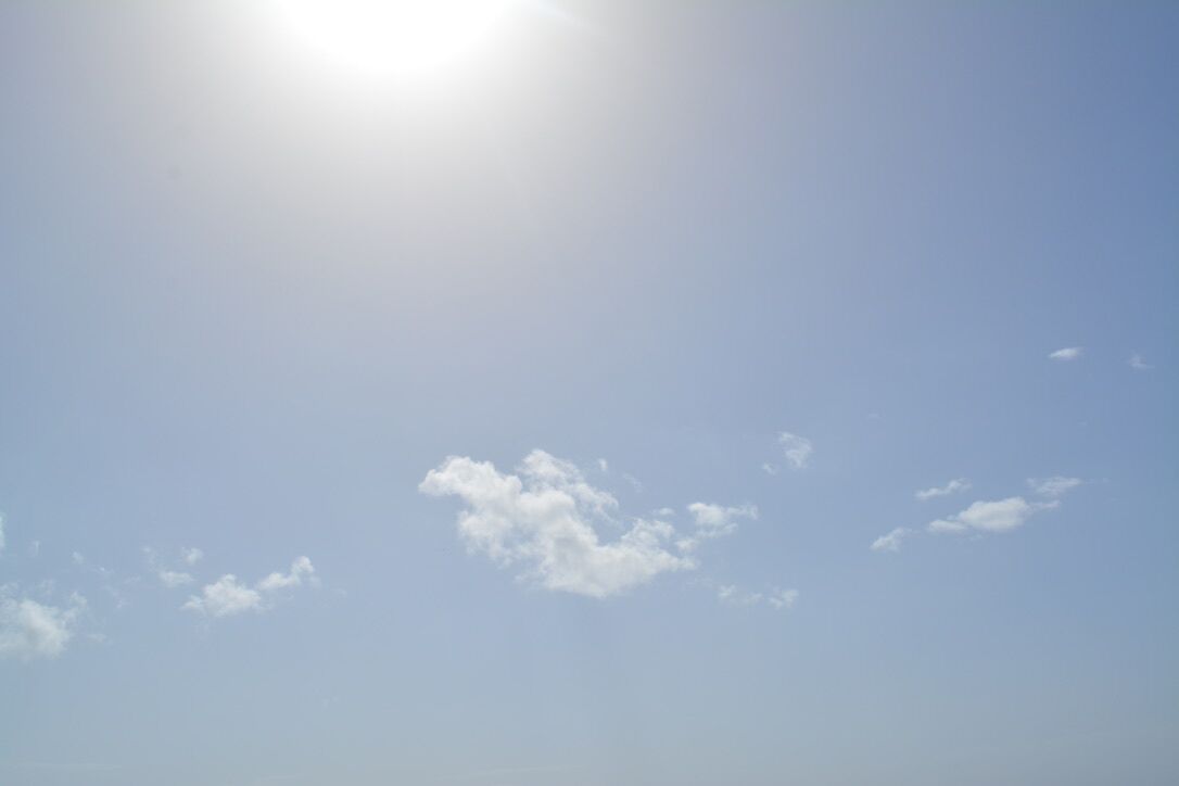 Céu limpo com o sol brilhando e algumas nuvens esparsas.