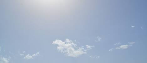 Céu limpo com o sol brilhando e algumas nuvens esparsas.