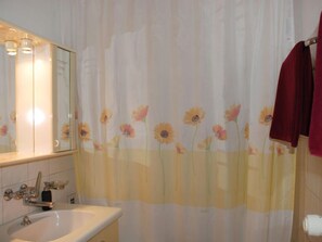 Een badkamer met een wastafel, spiegel en douchegordijn met bloemenmotieven.