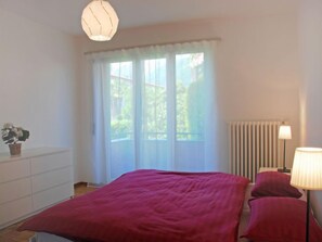 Een slaapkamer met een groot bed, een kaptafel, een radiator en een raam met gordijnen.
