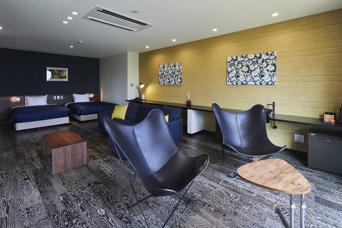 A modern hotel lobby with a sofa set, two black chairs, a wooden coffee table, and a reception desk.