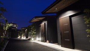 A modern building with large garage doors, a sloped roof, and a well-lit driveway at night. - Miyajima Hanarenoyado IBUKU Bettei (Hatsukaichi)