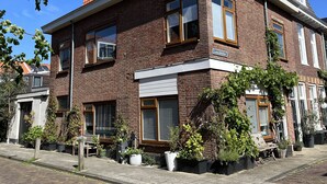 Ein zweistöckiges Backsteinhhaus mit rotem Ziegeldach, zahlreichen Fenstern und einem sichtbaren Balkon.