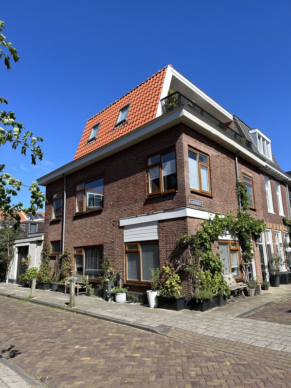 A two-story brick house with a red-tiled roof, multiple windows, and a visible balcony.