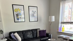 Ein modernes Wohnzimmer mit einer schwarzen Ledersofa, einem gemusterten Teppich und zwei gerahmten Kunstwerken an der Wand.