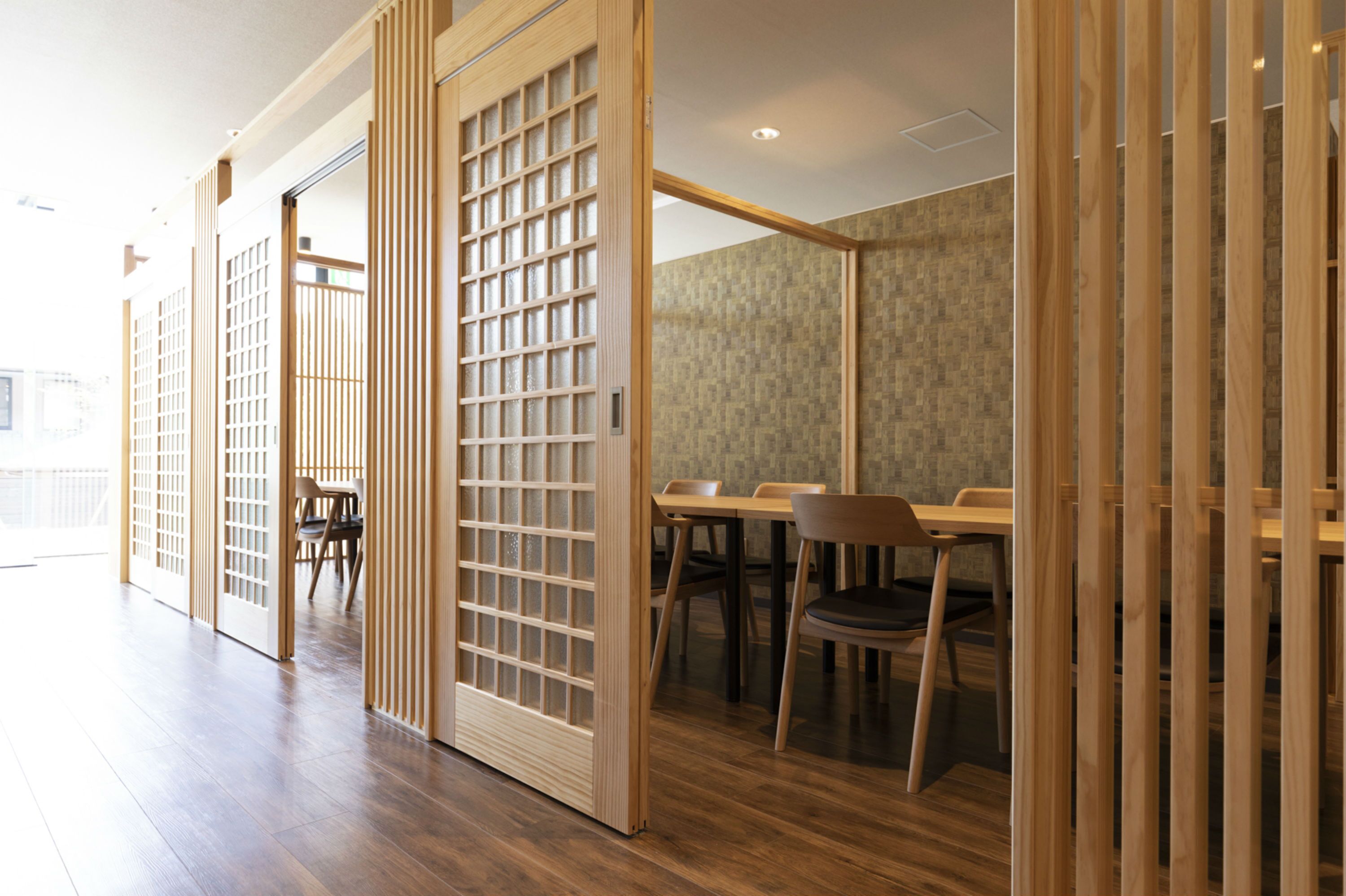 Um quarto japonês tradicional com portas deslizantes, piso de madeira e uma área de jantar com cadeiras e mesas.