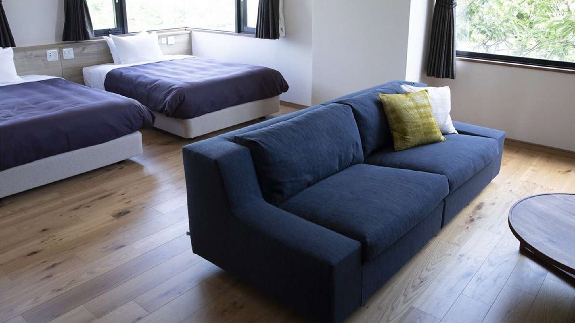 Une chambre moderne avec deux lits simples, un canapé bleu et une table ronde.