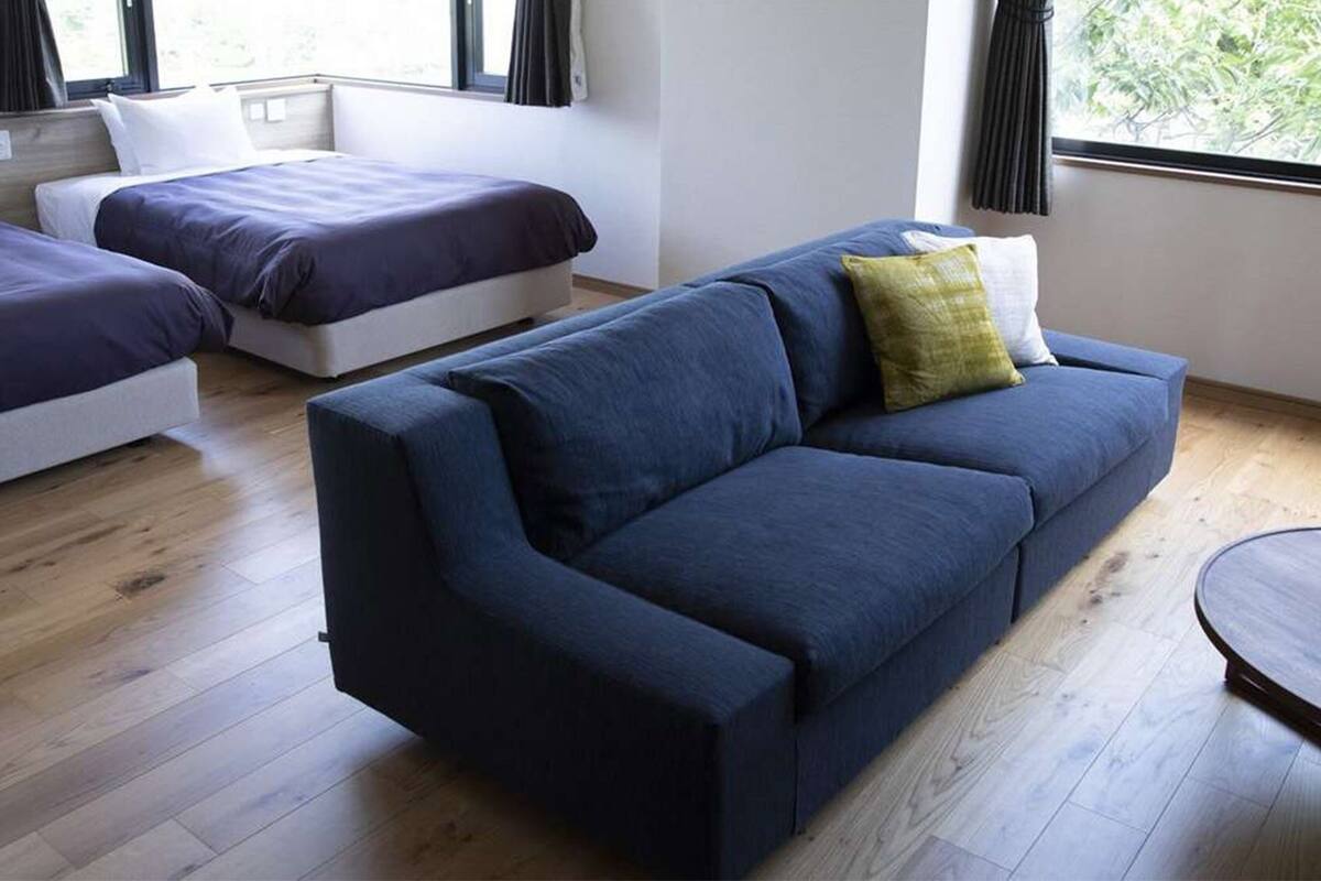 Een moderne kamer met twee eenpersoonsbedden, een blauwe bank en een ronde tafel.