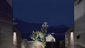 Un bâtiment moderne avec un arbre au centre, entouré de murs aux lignes horizontales et avec une montagne en arrière-plan.