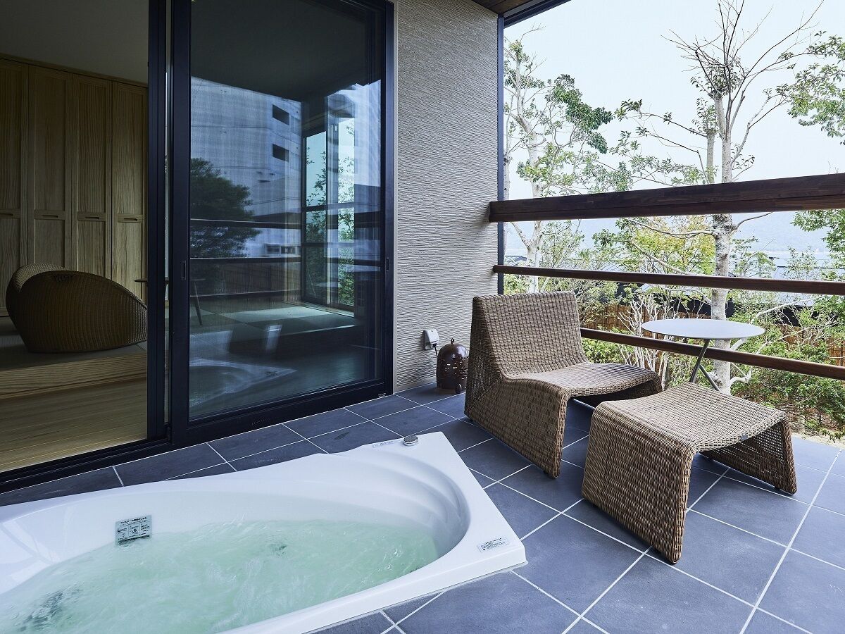 A modern outdoor area with a hot tub, wicker furniture, and a glass door leading to a room.