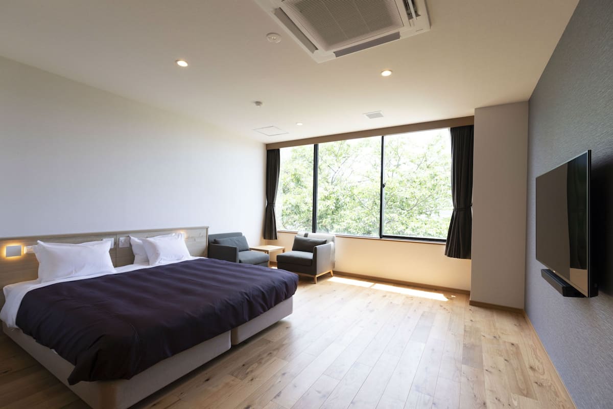 Een moderne hotelkamer met een groot bed, een flatscreen televisie en een groot raam met uitzicht op bomen.