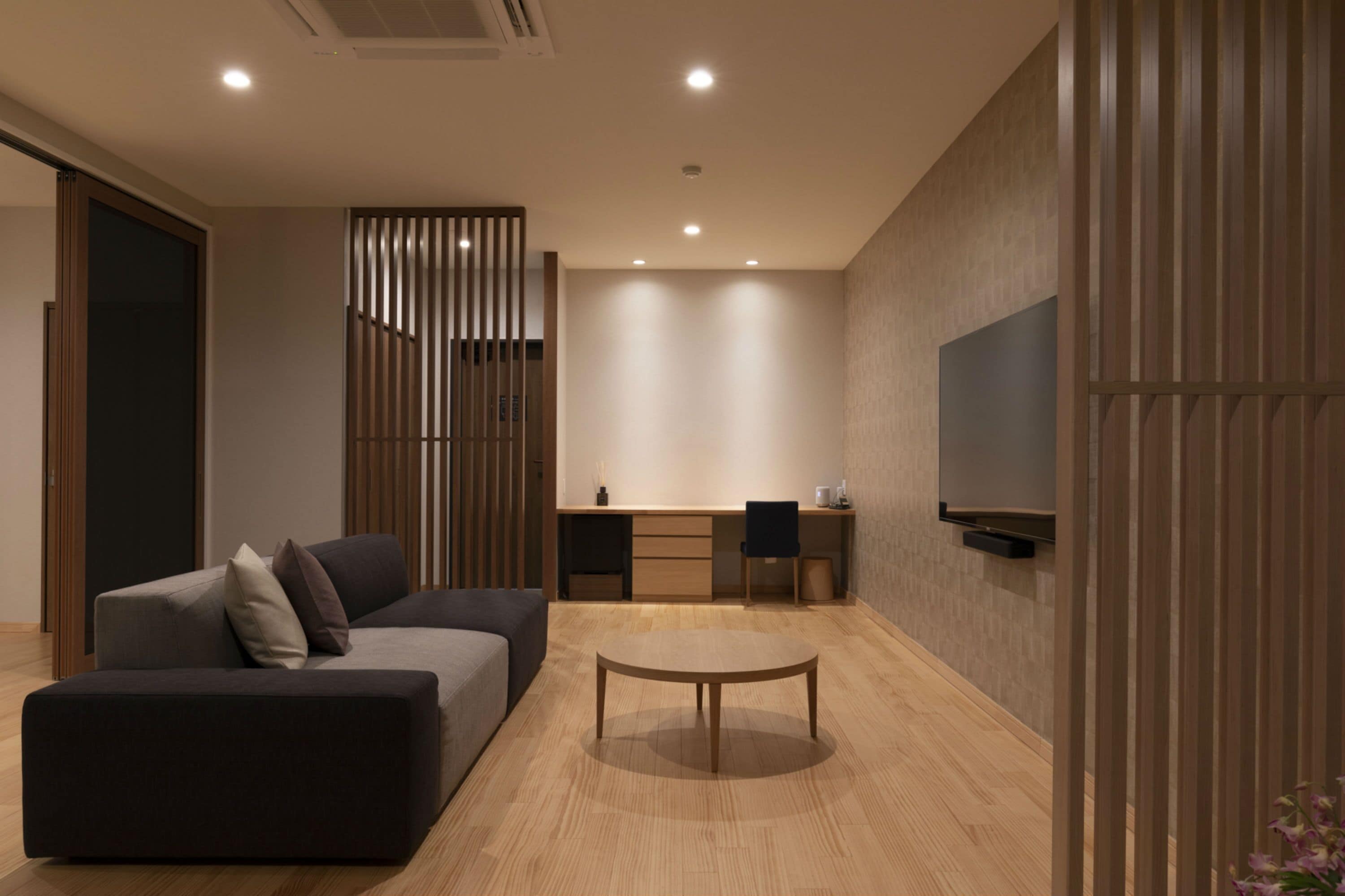 A modern living room with a sofa, a coffee table, a TV mounted on the wall, and a wooden partition.