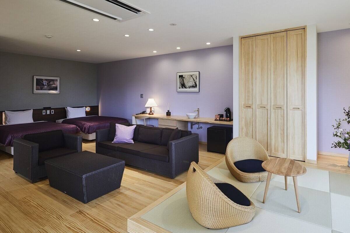 Een moderne hotelkamer met een bed, twee banken, een tafeltje, een stoel en een kledingkast.