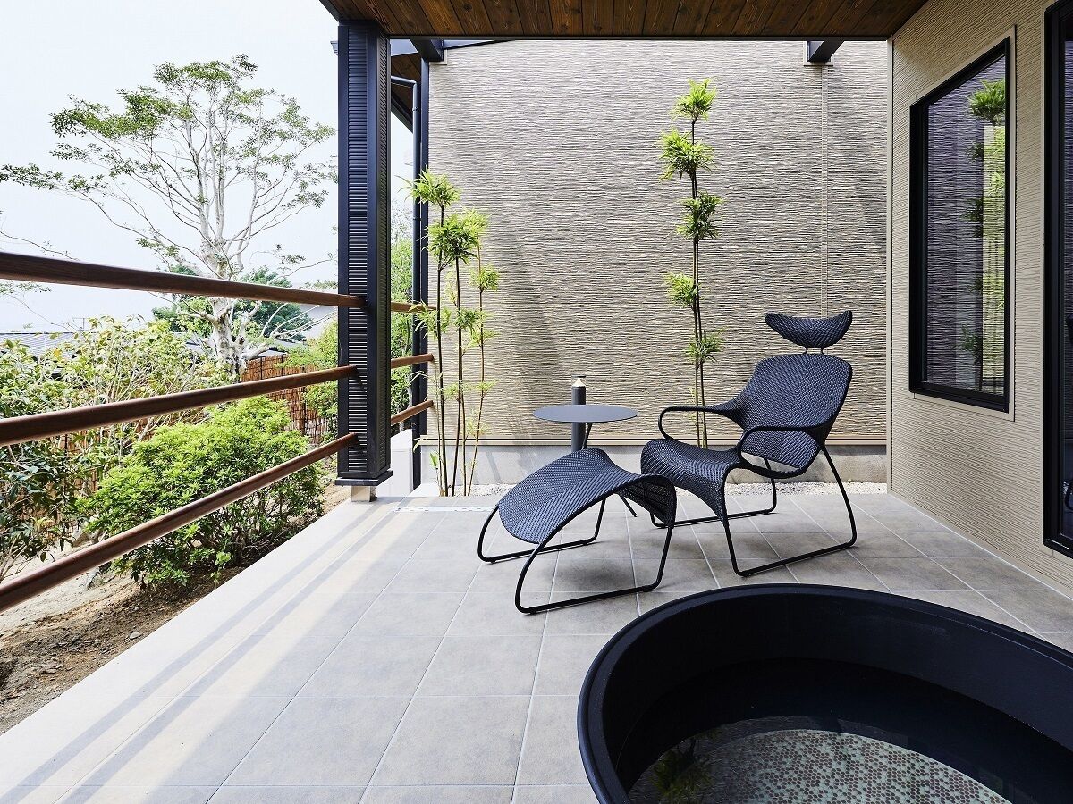 Un patio al aire libre con dos sillas de mimbre, una mesita, un muro de piedra y vistas a árboles.