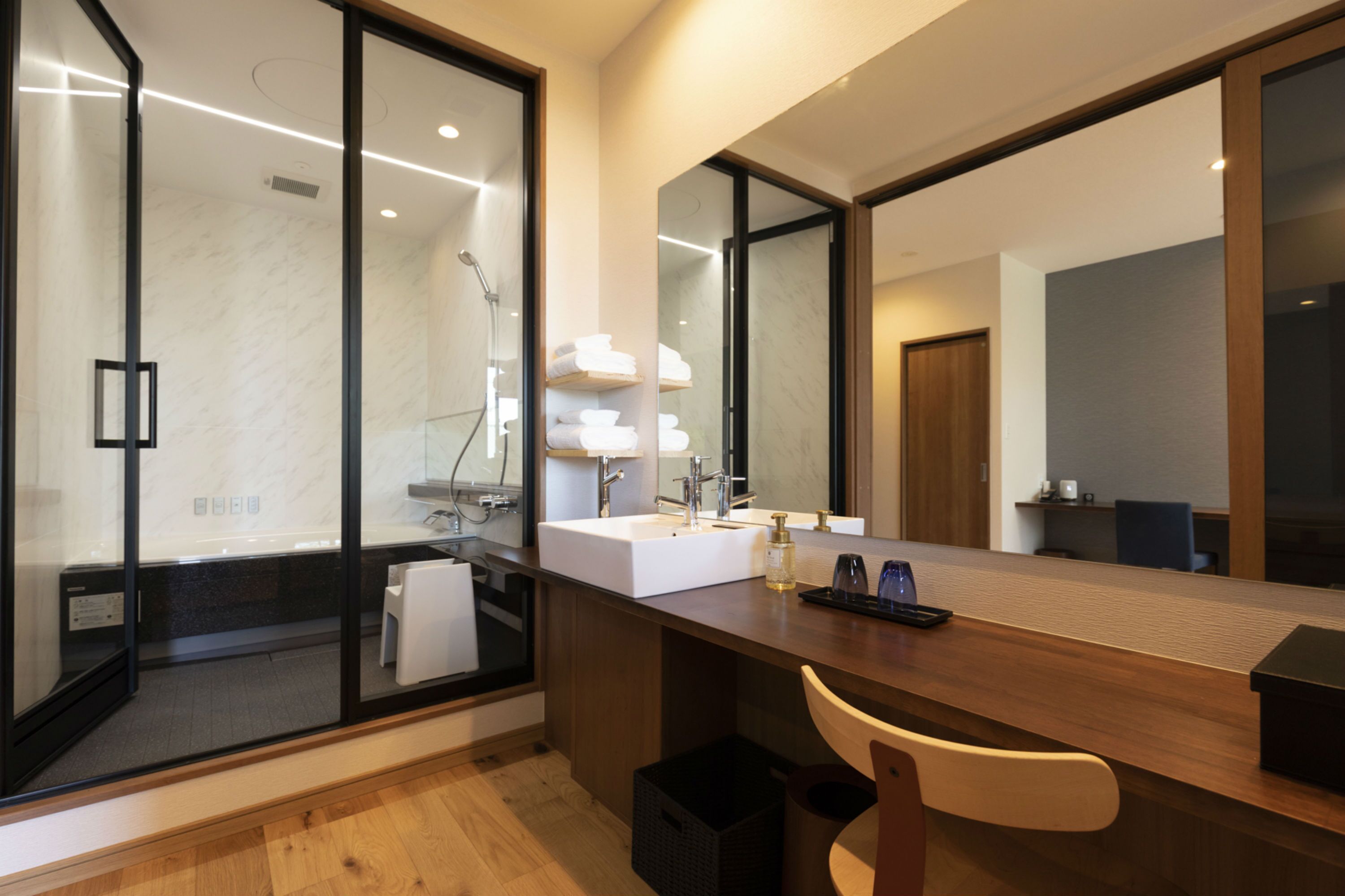 A modern bathroom with a glass shower enclosure, a large mirror, a wooden vanity, and a towel rack.