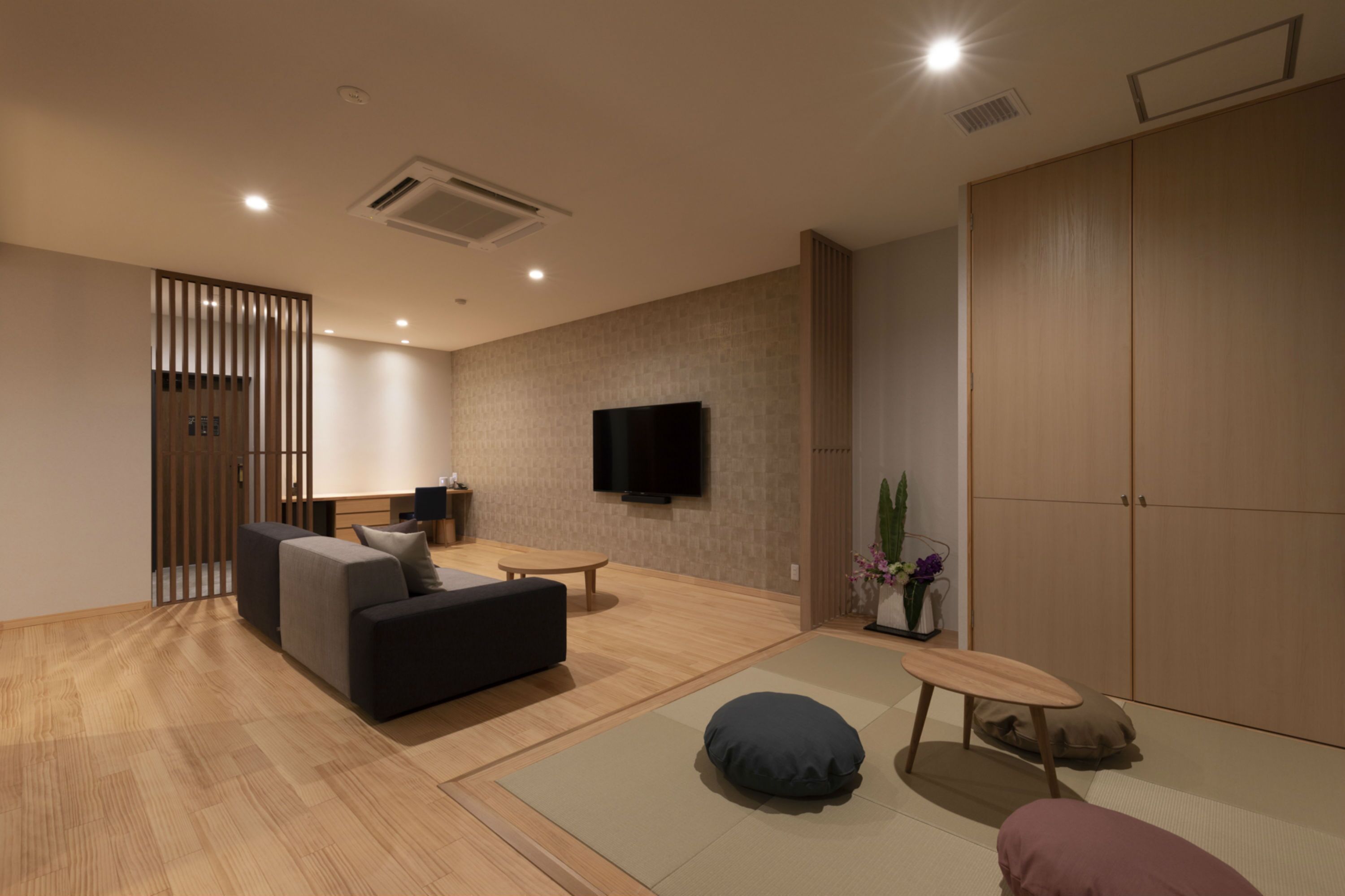 A modern living room with a sofa, a small table, a TV mounted on the wall, and a sliding door closet.