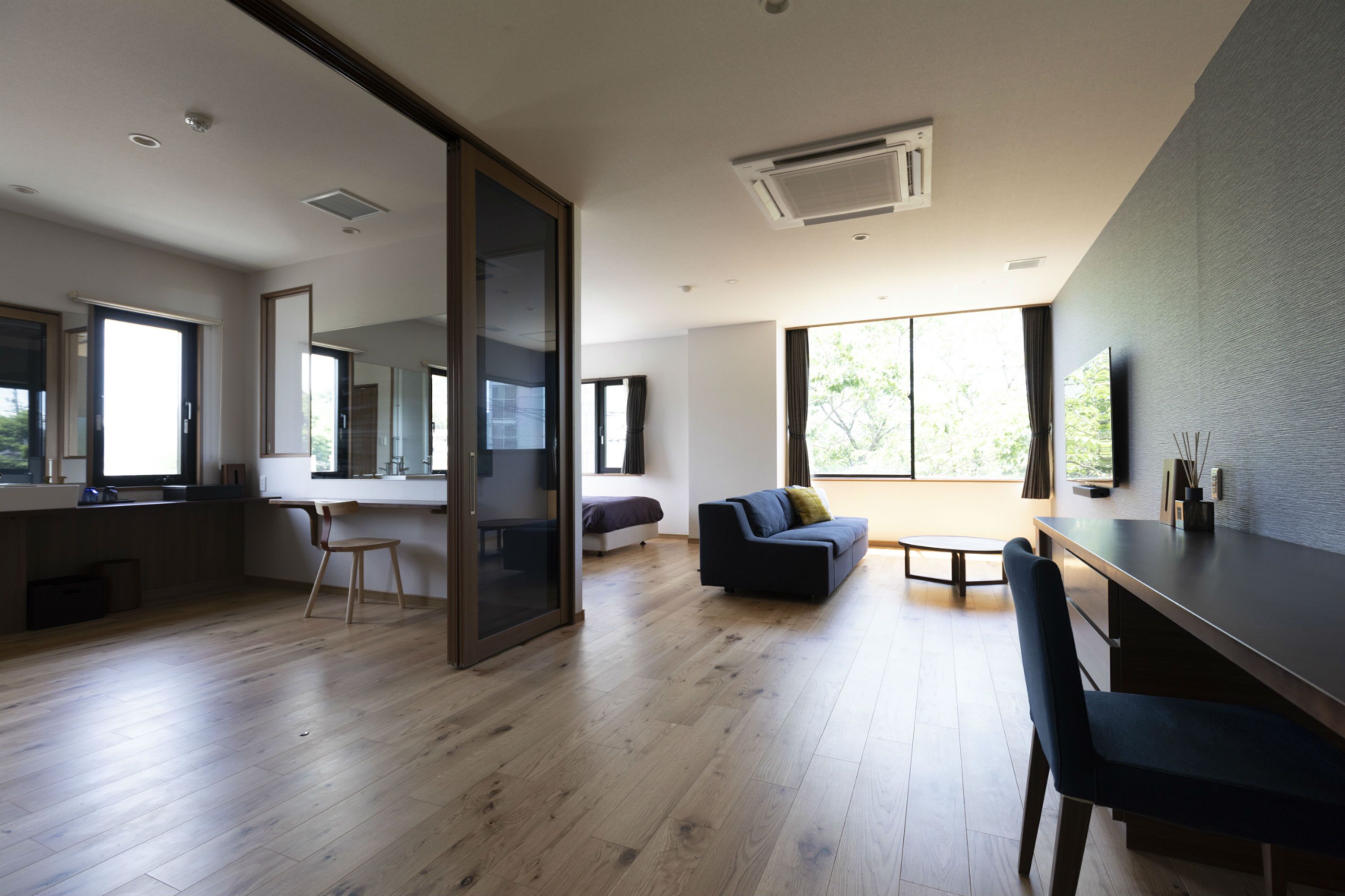 A modern living room with a wooden floor, a sofa, a dining table, and a TV.