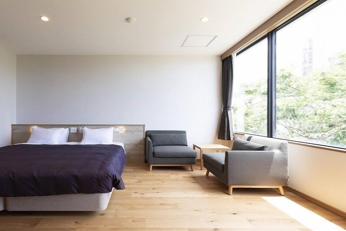 Een moderne hotelkamer met een groot bed, een kleine bank, een stoel en een groot raam met uitzicht op het omliggende landschap.
