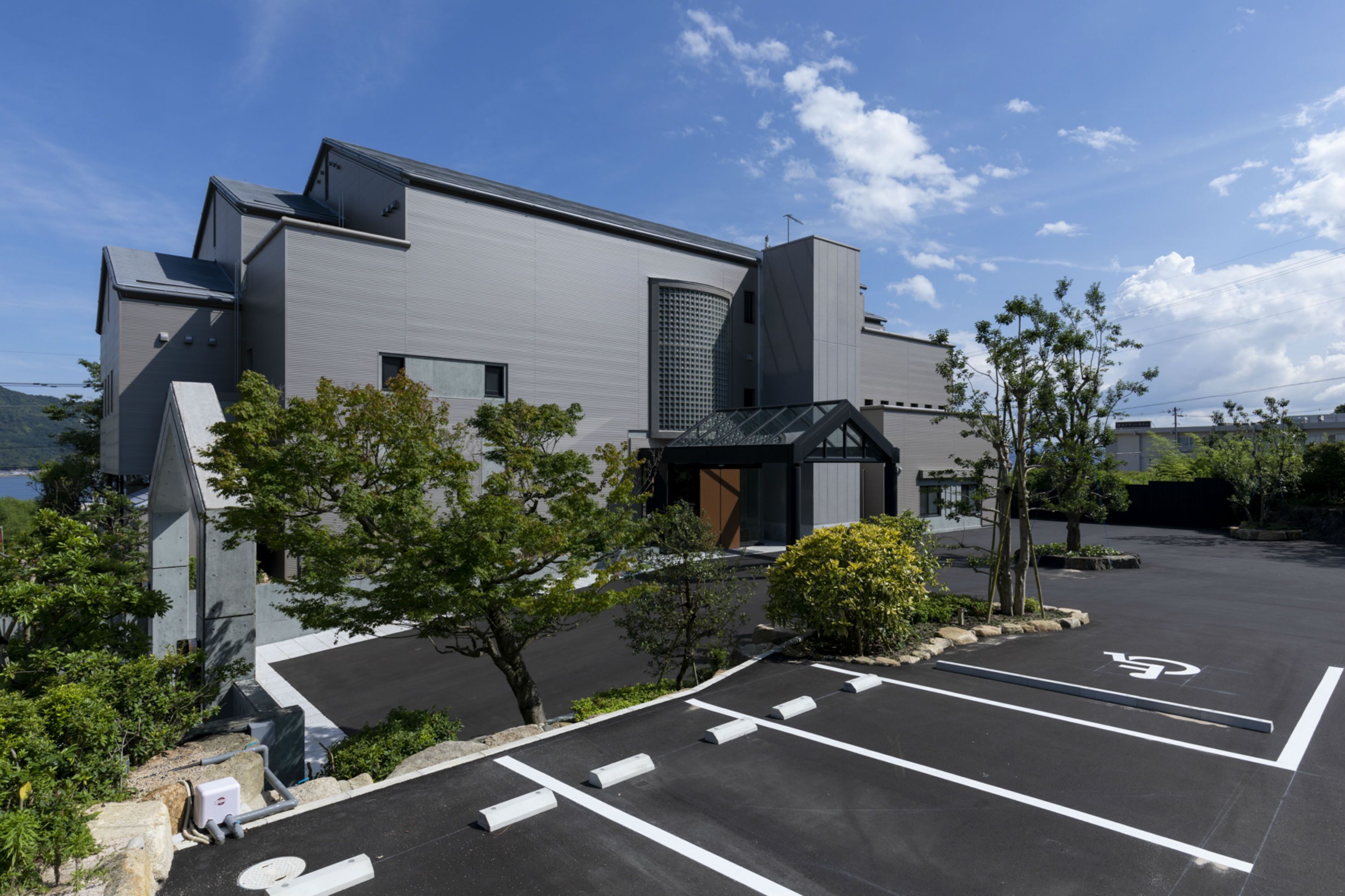 A modern building with a parking lot, trees, and a clear sky.