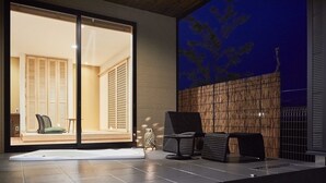 Un intérieur moderne avec une porte-fenêtre coulissante donnant sur un balcon, un coin salon avec des fauteuils et un mur à texture.