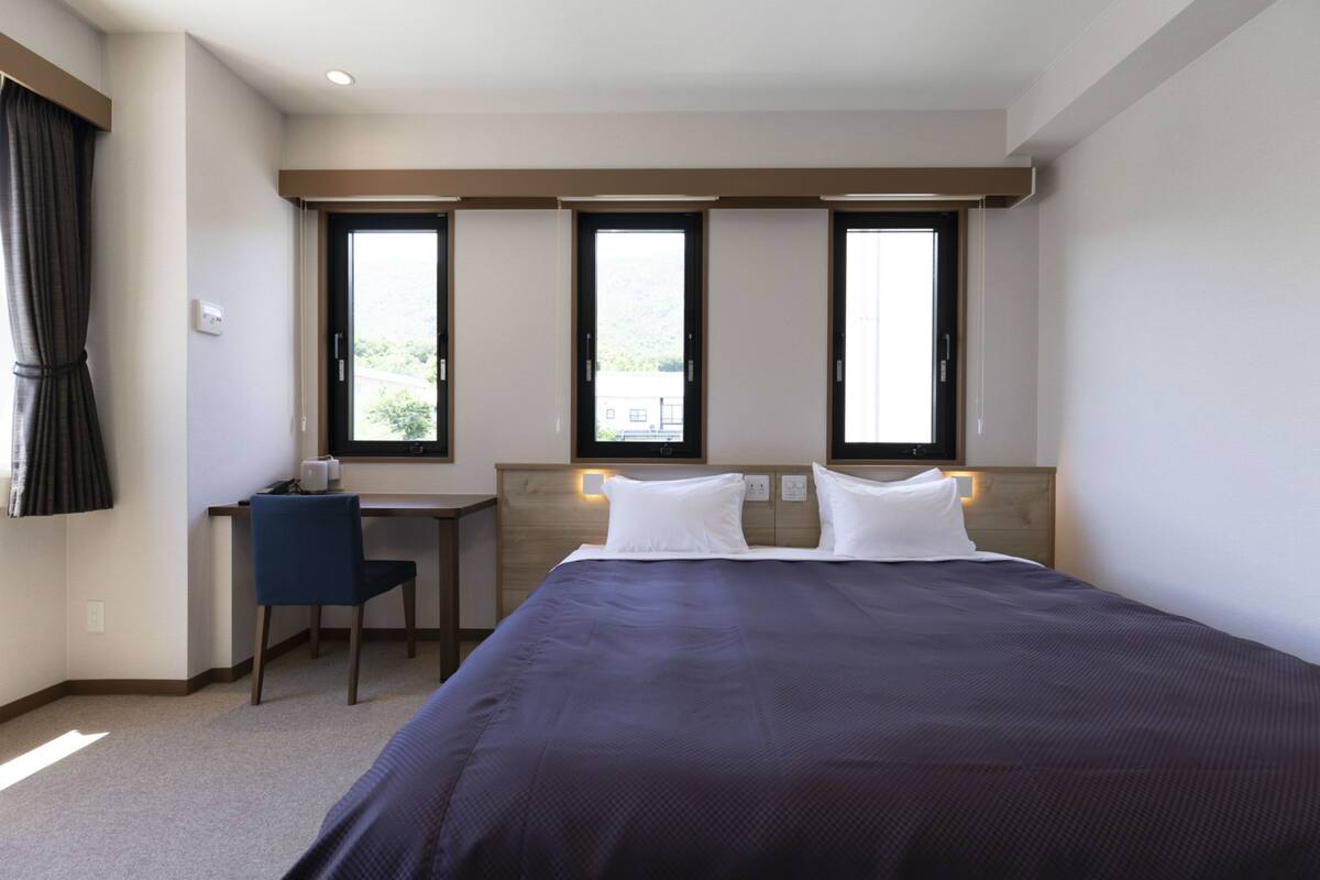 Een hotelkamer met een groot bed, een bureau en twee ramen.
