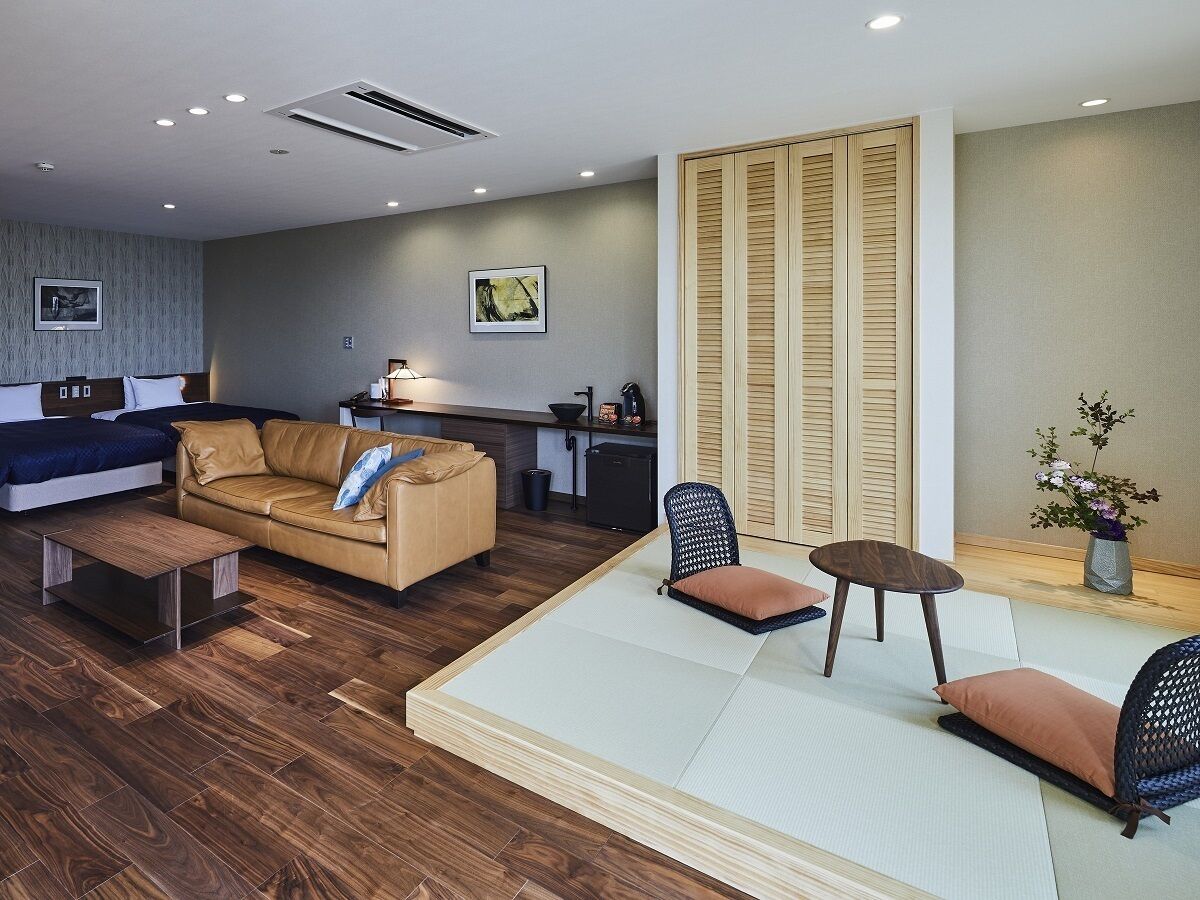 A modern hotel room with a sofa, a small table, a chair, and a tatami mat area.