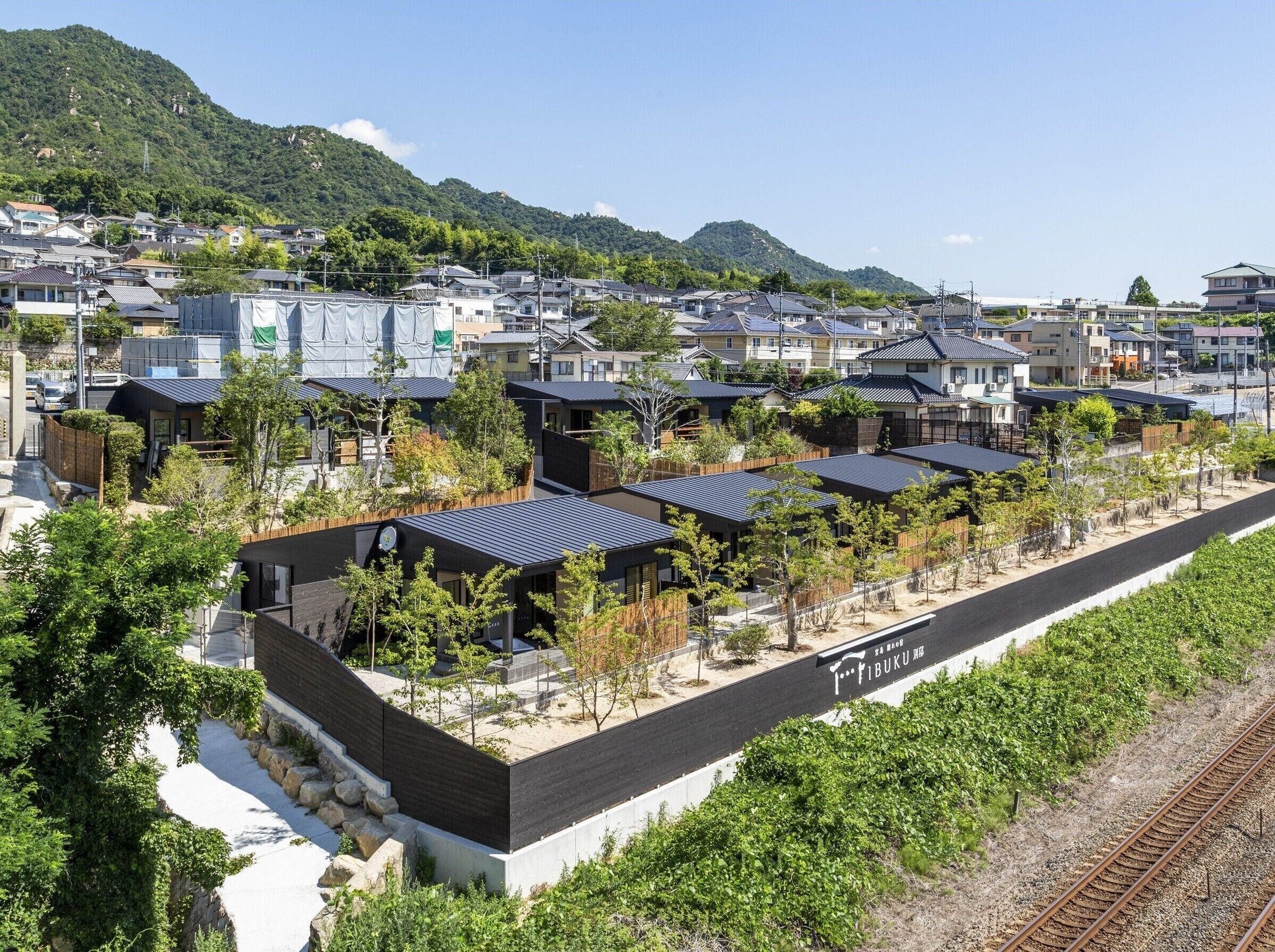 A residential area with modern houses, a train track, and a mountainous backdrop.