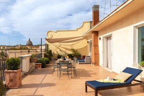 A rooftop terrace with a dining table, chairs, a lounge chair, potted plants, and a view of a dome in the distance.