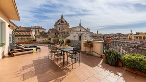Eine Dachterrasse mit Esstisch, Stühlen, Liegestuhl und Kübelpflanzen.