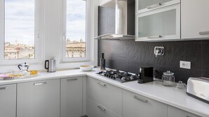 Eine moderne Küche mit Gasherd, Kaffeemaschine und Blick auf die Stadt durch große Fenster.