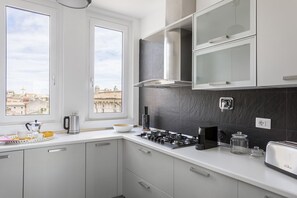 A modern kitchen with a gas stove, a coffee maker, and a view of the city through large windows.